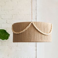 a wooden beaded light fixture hanging from a brick wall next to a green plant