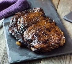 a piece of meat sitting on top of a black plate next to a purple napkin