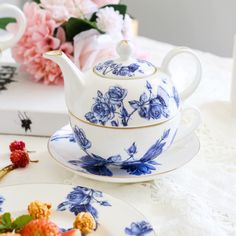 a blue and white tea set on a table with pink flowers in the back ground