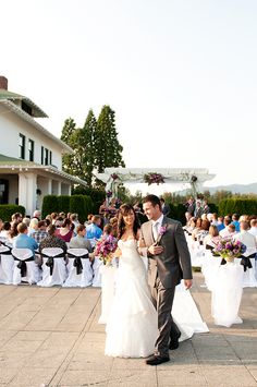 a bride and groom walking down the aisle at their wedding ceremony in front of an outdoor venue