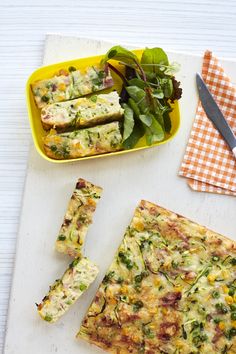 a table topped with slices of pizza next to a bowl of greens and a knife