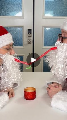 two men dressed as santa claus sitting at a table with a candle in front of them