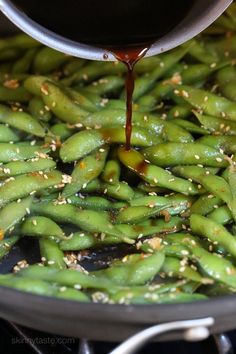 green beans being cooked in a pan with sesame seeds on the side and sauce being poured over them