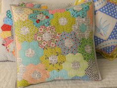 two colorful pillows sitting on top of a bed next to each other, one has a patchwork design