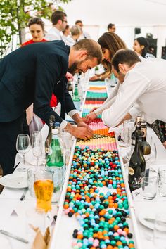 two men are decorating a table with colorful candies and wine glasses on it