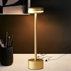 a lamp that is on top of a table next to a cup with pens and pencils in it