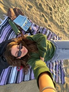 a woman laying on top of a beach next to a book