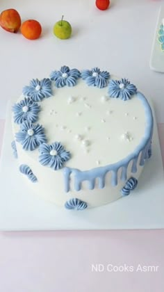 a white cake with blue icing sitting on top of a table next to fruit