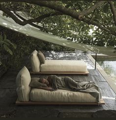 a person laying on top of a couch under a tree next to a swimming pool