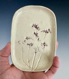 a hand holding a white plate with flowers on it