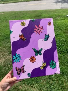 a hand holding up a purple square with colorful butterflies on it in the grass next to a street