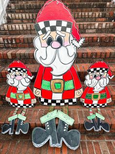 three paper cutouts of santa claus and elves on the steps in front of a brick building