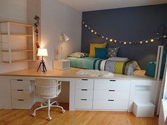 a room with a bed, desk and shelves on the wall next to a window