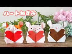 three origami rabbits with hearts in their hands on a wooden table next to flowers