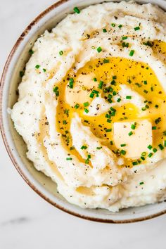 mashed potatoes topped with butter and chives in a bowl on a marble surface