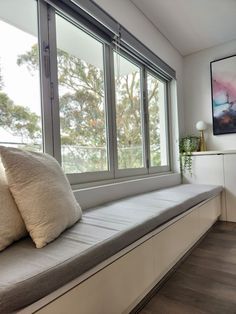 a window seat with two pillows on it in front of a large window overlooking the trees