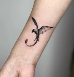 a small tattoo on the wrist of a woman's arm with a dragon flying over it