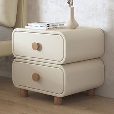 a white table with two drawers and a vase on top, next to a bed