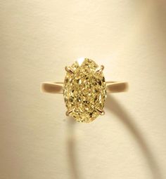 a yellow diamond ring sitting on top of a white table next to a light colored wall