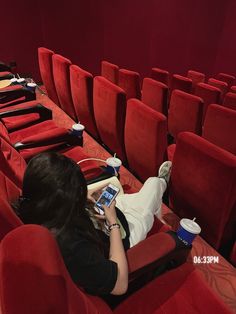 a woman laying on the red seats in an empty theater looking at her cell phone