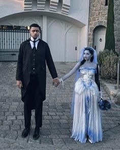 a man and woman dressed up as corpse brides holding hands in front of a castle