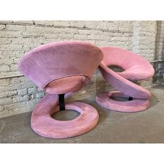 two pink chairs sitting next to each other in front of a brick wall and floor