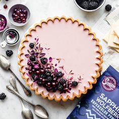 a tart with berries and blackberries on it next to silverware, spoons and cheese