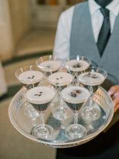 a man holding a tray with wine glasses and buttons on it in front of him