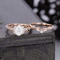 two wedding rings with diamond accents on top of each other in front of a wooden box