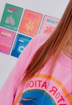 a girl with long hair wearing a pink shirt and looking at her cell phone while standing in front of posters on the wall