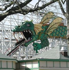 a green and yellow dragon statue on top of a roller coaster at a theme park