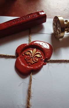 a red wax stamp sitting on top of a piece of paper next to a pen