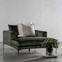 a green velvet chaise lounge chair with two pillows on it and a plant in the corner