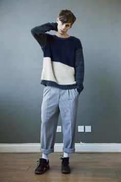 a young man standing in front of a gray wall with his hands on his head