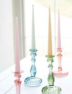 four candles are lined up on a table in different shades of pink, green and blue