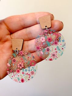 a person is holding two small earrings in their left hand and the other one has flowers on it