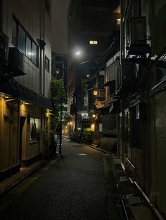 an alley way at night with lights on and buildings lining the street in the background