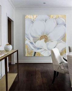 a dining room with a large white flower painting on the wall and wooden flooring