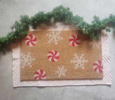 a door mat with candy canes and snowflakes on it next to christmas greenery