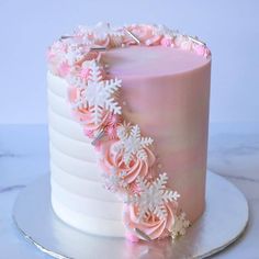 a pink frosted cake decorated with flowers and snowflakes on a silver platter