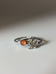 a silver ring with an orange stone and leaf on the front, sitting on a white surface