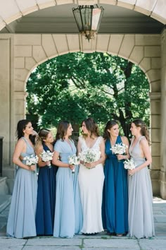 a group of women standing next to each other in front of a stone arch holding bouquets