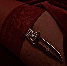 there is a large knife on top of a red cloth with an intricate design around it