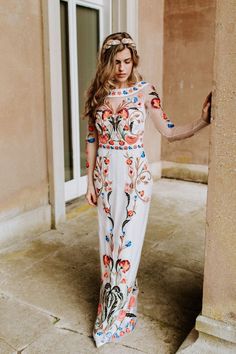 a woman in a long dress is standing by a pillar and looking at the camera