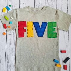 a t - shirt with the word five spelled out in lego letters, surrounded by toys