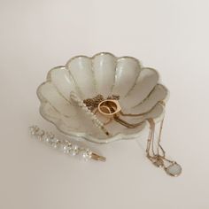 two wedding rings in a shell shaped dish with pearls and a necklace on the side