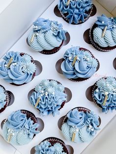 cupcakes with blue frosting and decorations in a white box on a table