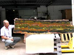 a man kneeling down next to a large piece of art in a garage with another person looking at it