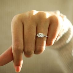 a woman's hand with a diamond ring on her finger, pointing at the camera