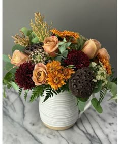 a white vase filled with lots of flowers on top of a marble countertop next to a wall